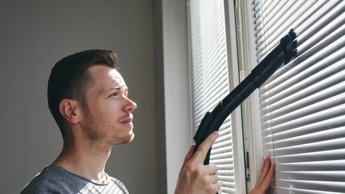 Man using a vacuum attachment to clean window blinds during a rental property bond clean