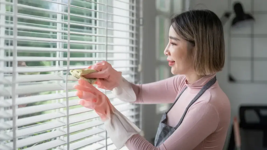 Cleaner wiping individual blind slats with a cloth during a bond clean in a Queensland rental property