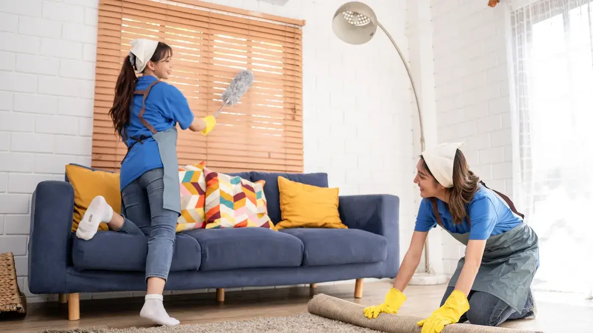 Cleaners dusting Venetian blinds and rolling a rug during a residential bond clean