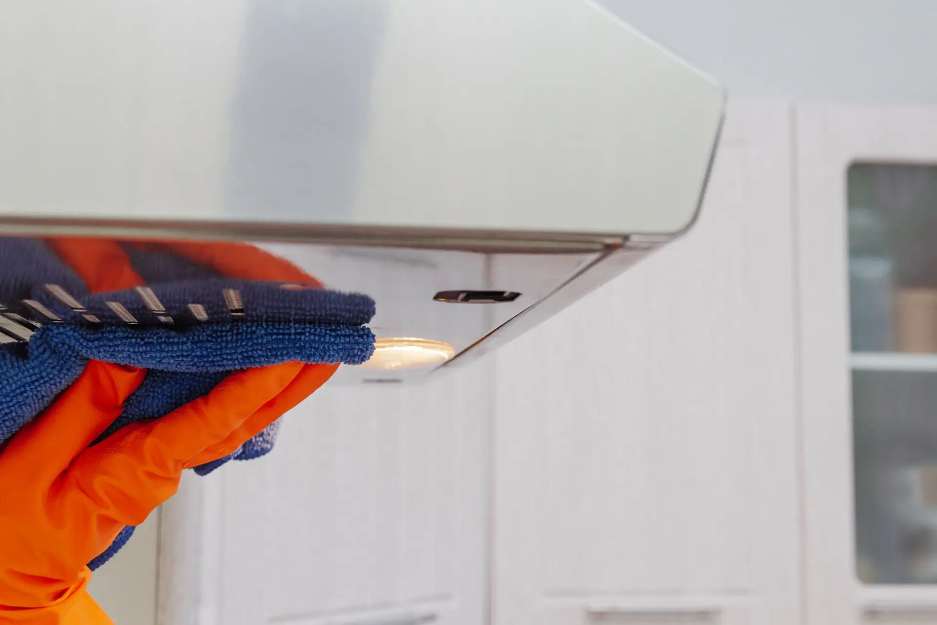 An Urgent Pro bond cleaning provider in Brisbane removing the rangehood filter and cleaning the inside of the oven targeting areas checked in bond inspections, with professional equipment visible in a realistic local service setting
