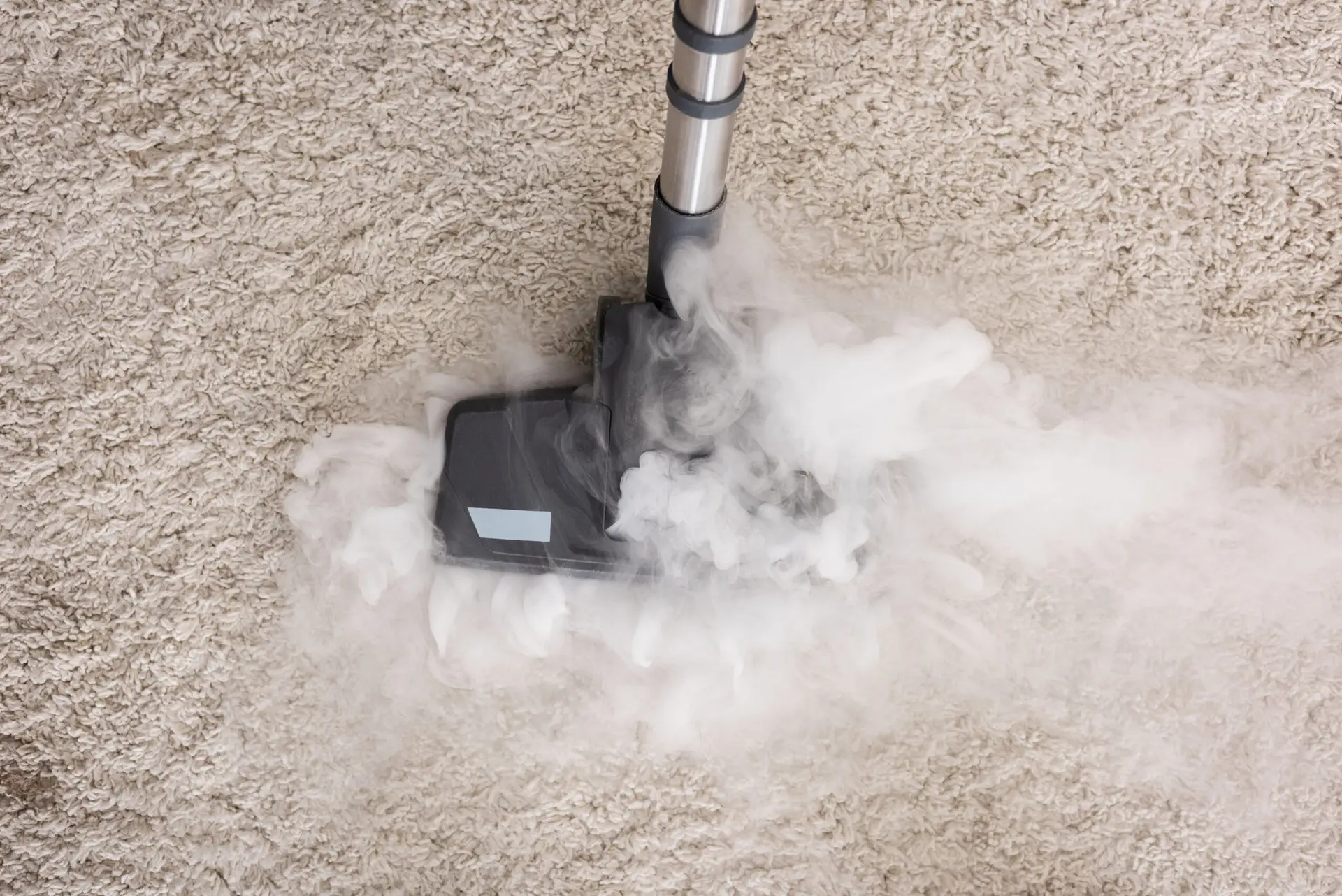 An Urgent Pro carpet cleaning provider in Melbourne applying a pre-treatment spray to a visible carpet stain before steam cleaning, with professional equipment visible in a realistic local service setting