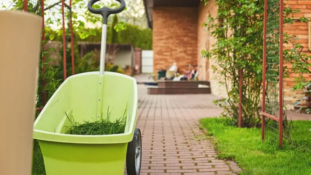 Garden cart with fresh grass clippings on a terracotta brick-paved path beside a maintained garden