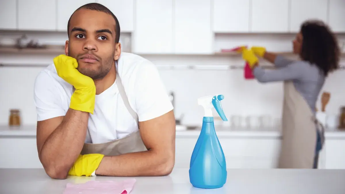 Tenant wearing rubber gloves pauses at a kitchen counter with cleaning spray and a cloth