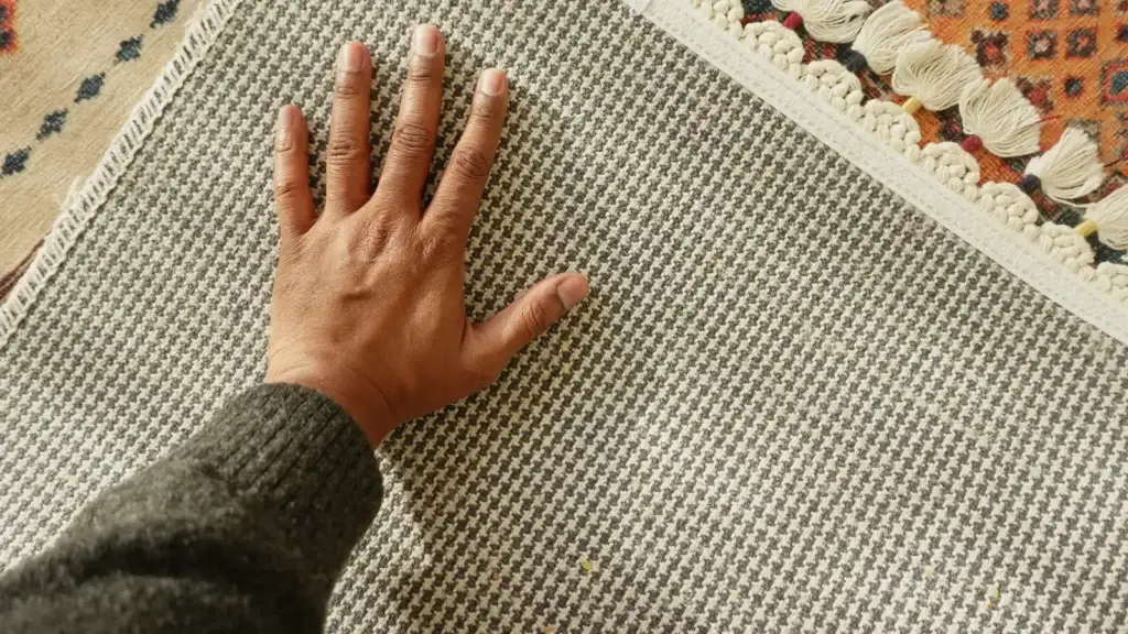 Hand pressed flat on grey houndstooth rug pile with tasselled patterned rug visible in background