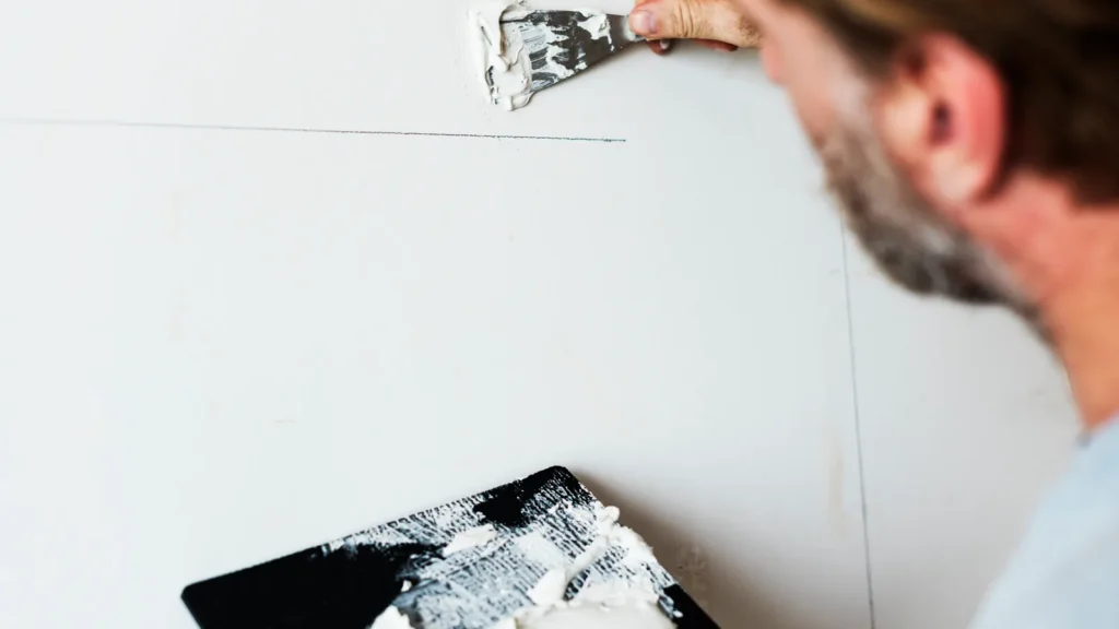 Tradesperson applying jointing compound to a plasterboard wall repair using a broad-blade spatula and mud board