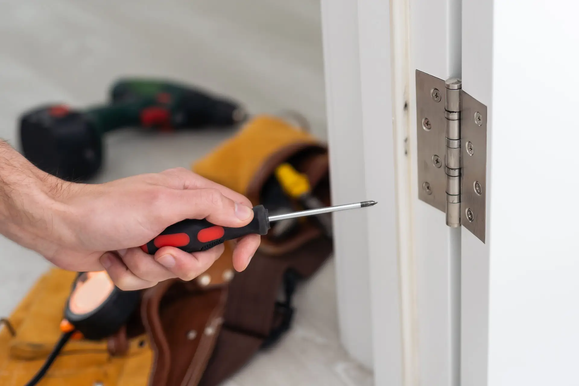 An Urgent Pro handyman provider in Brisbane adjusting sticking door hinges and planing a swollen door frame to allow smooth opening, with professional equipment visible in a realistic local service setting