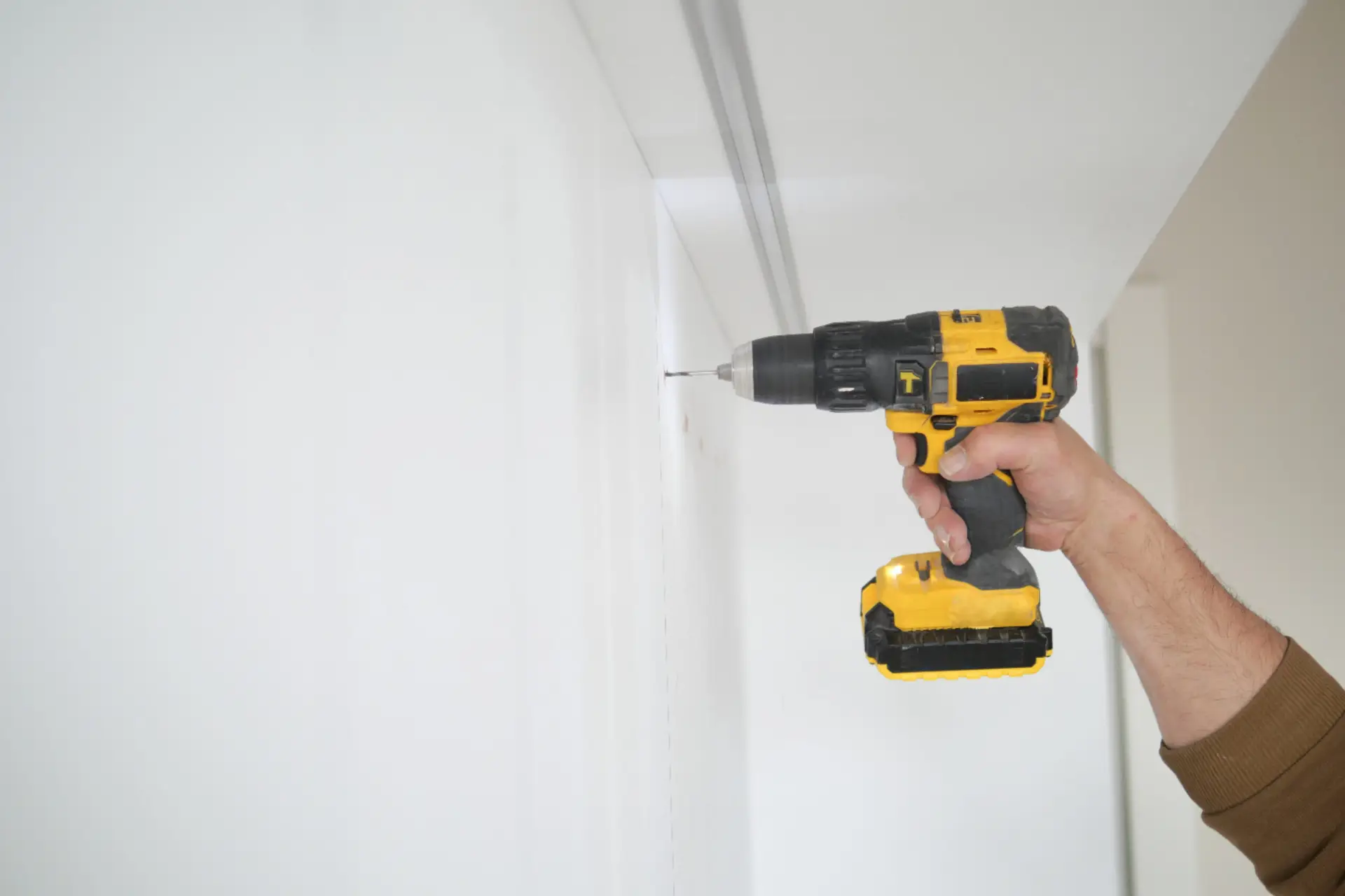 An Urgent Pro handyman provider in Gold Coast drilling into a wall to mount a TV bracket using a stud finder and spirit level, with professional equipment visible in a realistic local service setting