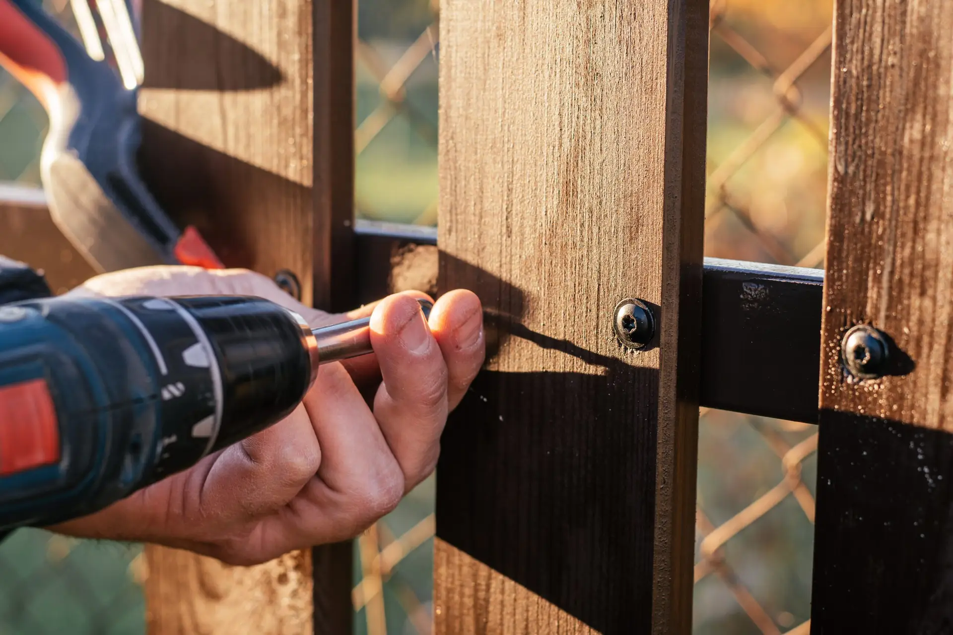 An Urgent Pro handyman provider in Gold Coast repairing a damaged fence paling and securing a loose post with a drill and treated timber, with professional equipment visible in a realistic local service setting