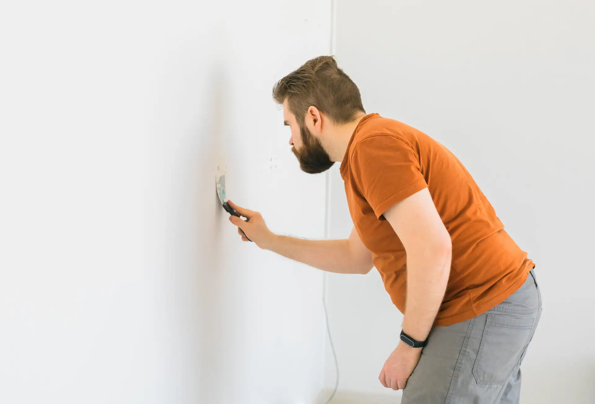 An Urgent Pro handyman provider in Gold Coast applying plaster filler to a wall hole, sanding it smooth and priming before repainting, with professional equipment visible in a realistic local service setting