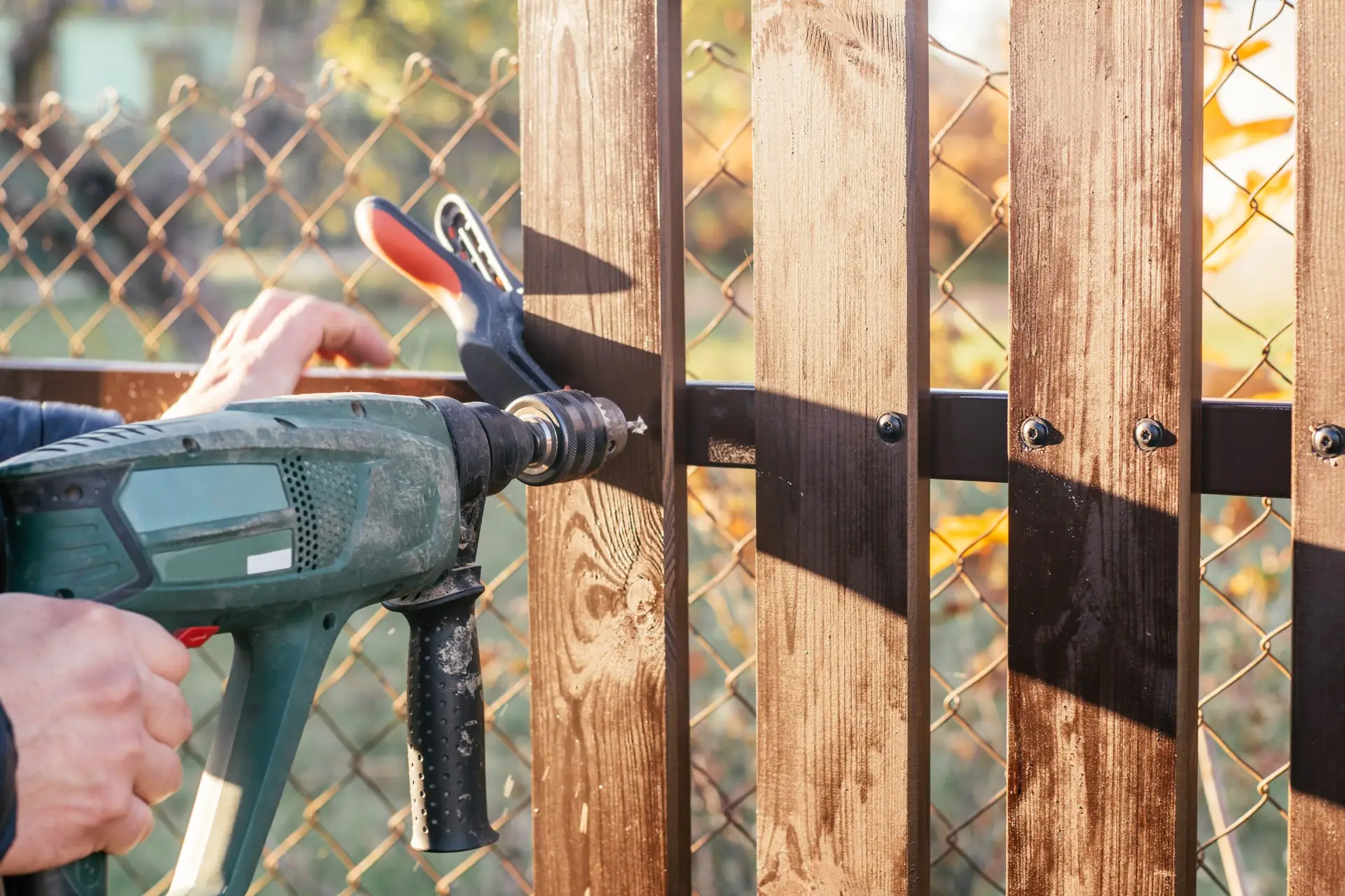An Urgent Pro handyman provider in Perth repairing a damaged fence paling and securing a loose post with a drill and treated timber, with professional equipment visible in a realistic local service setting