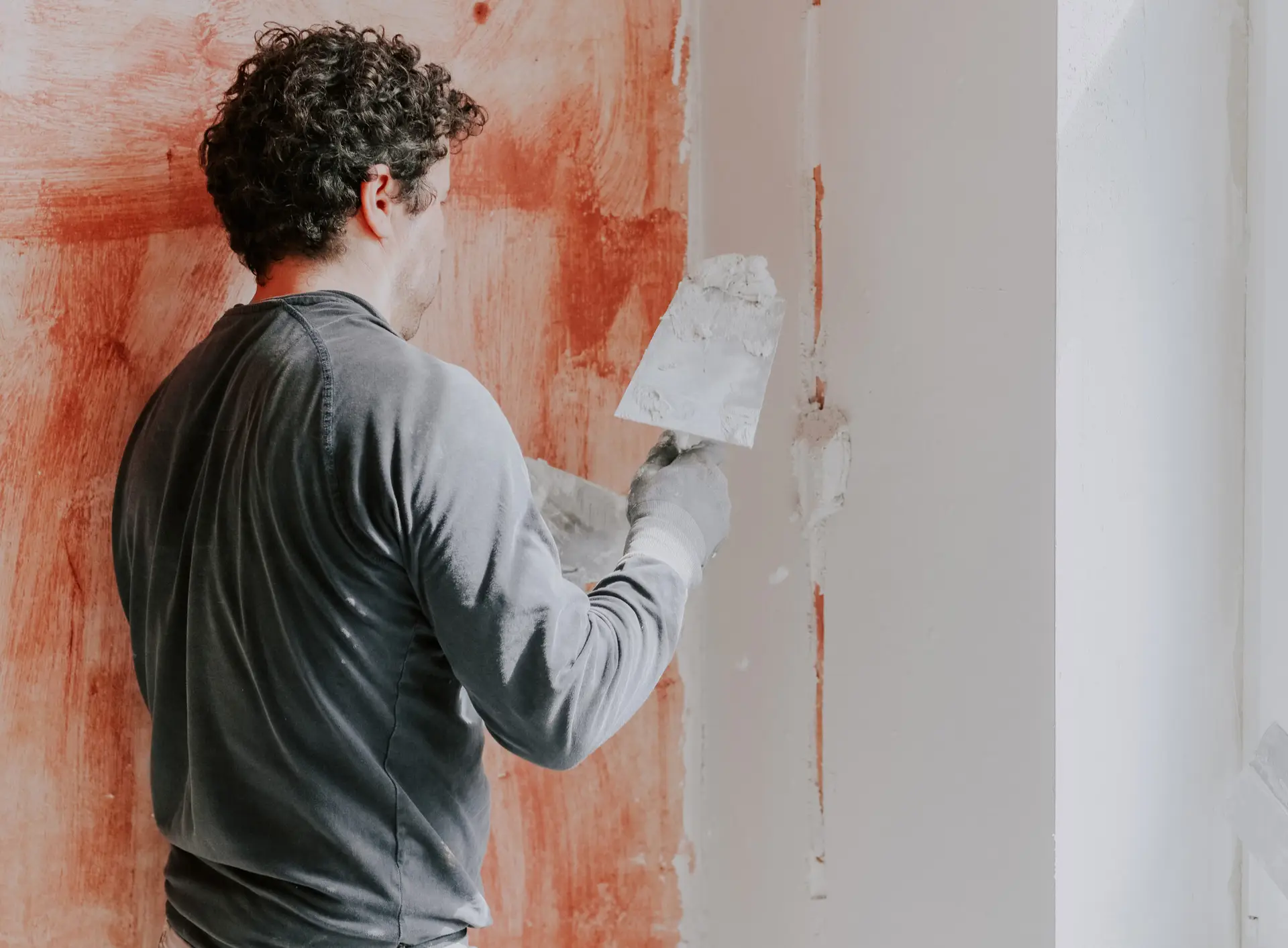 An Urgent Pro handyman provider in Sydney applying plaster filler to a wall hole, sanding it smooth and priming before repainting, with professional equipment visible in a realistic local service setting