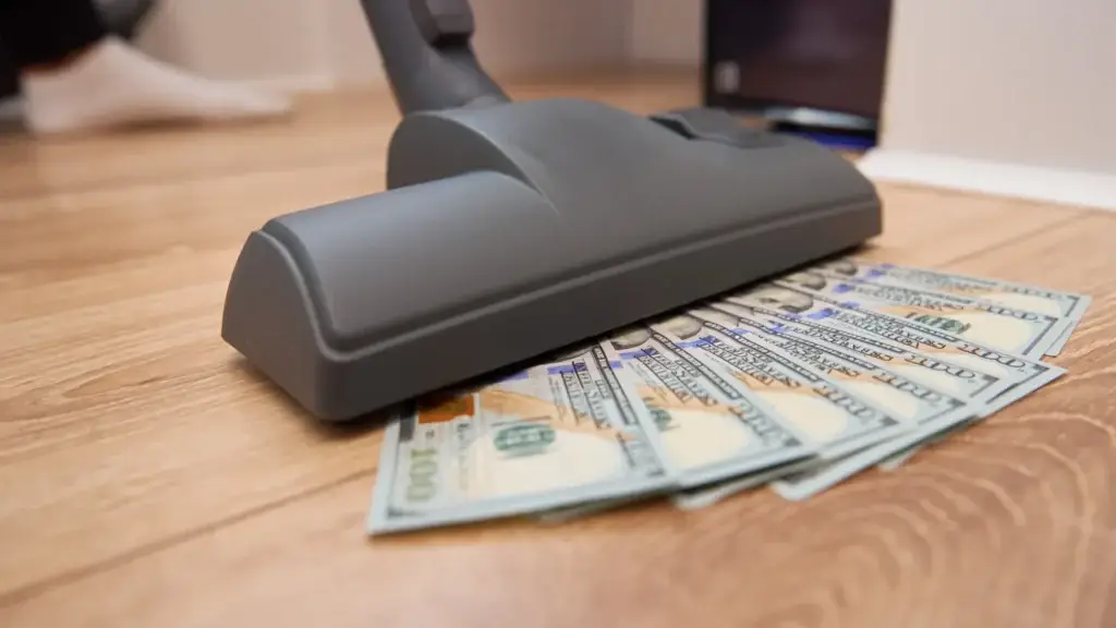 Vacuum cleaner floor head resting on banknotes fanned across a timber floor representing house cleaning cost
