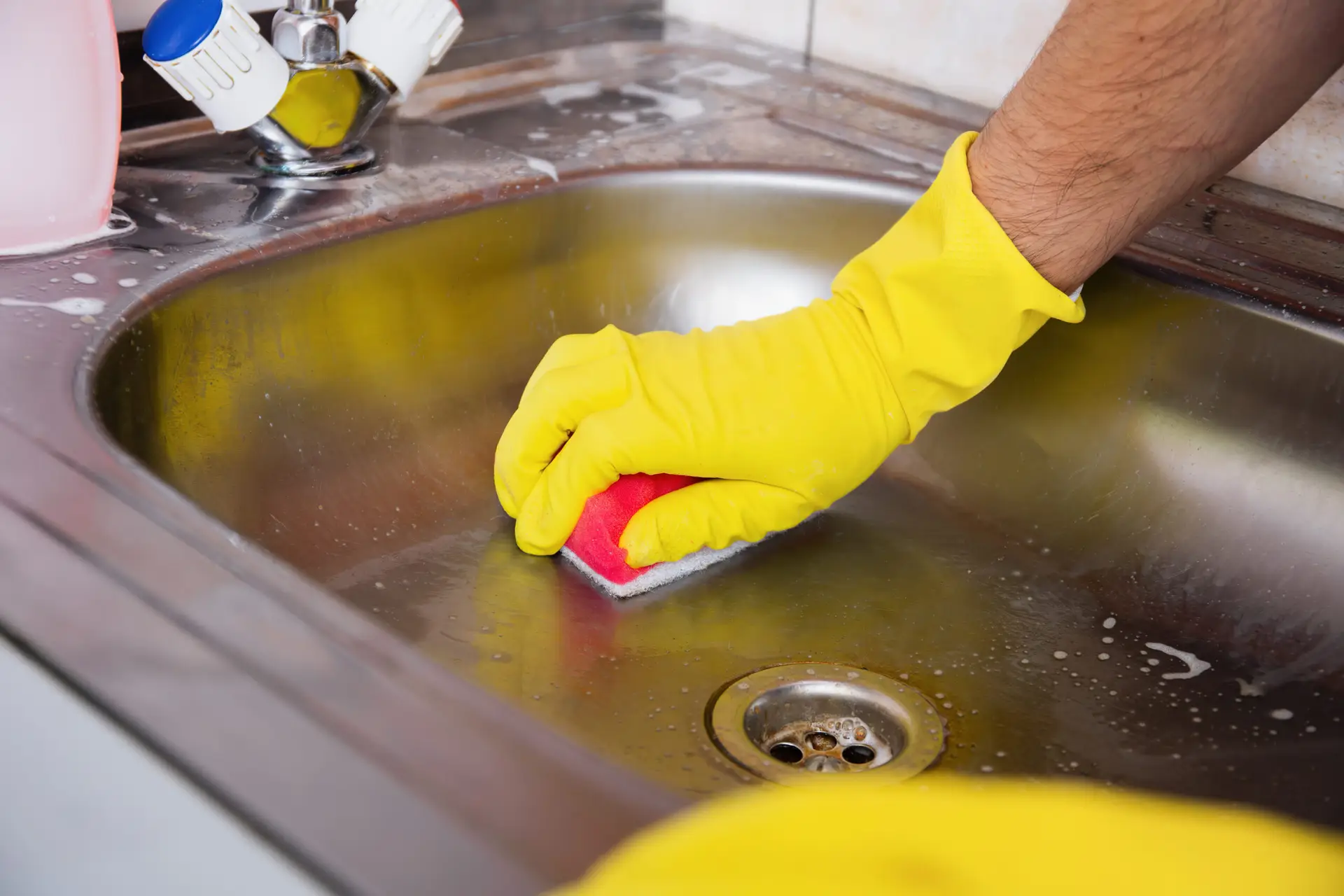 An Urgent Pro house cleaning provider in Gold Coast scrubbing the sink, wiping the stovetop and cleaning behind the taps in a Gold Coast family kitchen, with professional equipment visible in a realistic local service setting