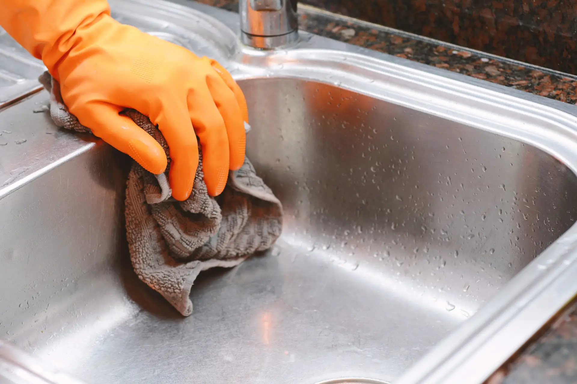 An Urgent Pro house cleaning provider in Melbourne scrubbing the sink, wiping the stovetop and cleaning behind the taps in a Melbourne family kitchen, with professional equipment visible in a realistic local service setting