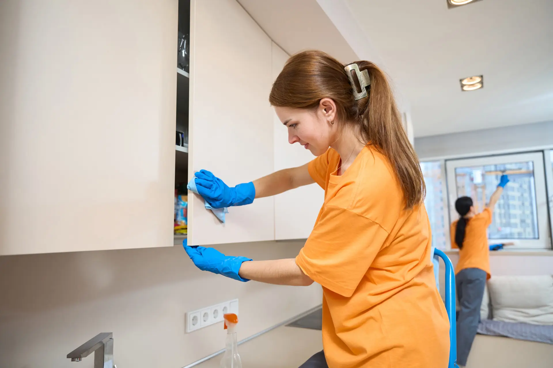 An Urgent Pro house cleaning provider in Perth wiping kitchen benches, appliance fronts and cupboard doors in an occupied Perth family home, with professional equipment visible in a realistic local service setting