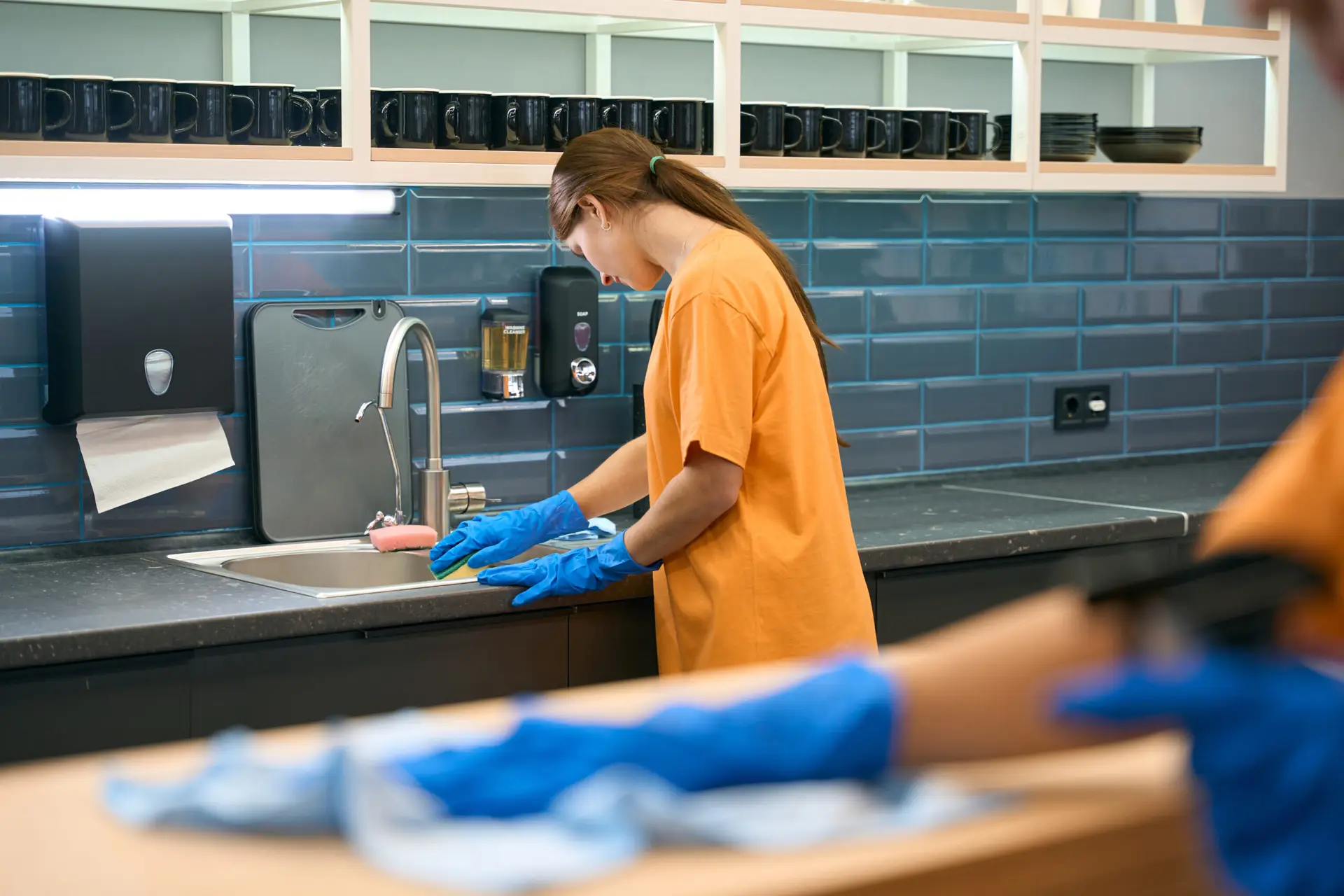 An Urgent Pro house cleaning provider in Sydney wiping kitchen benches, appliance fronts and cupboard doors in an occupied Sydney family home, with professional equipment visible in a realistic local service setting