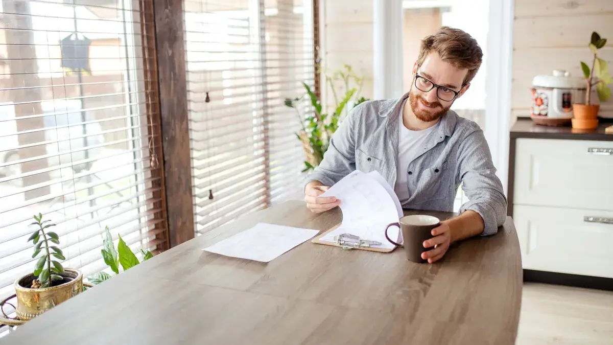 Man with glasses reviewing removalist paperwork at a timber dining table with a coffee mug beside him