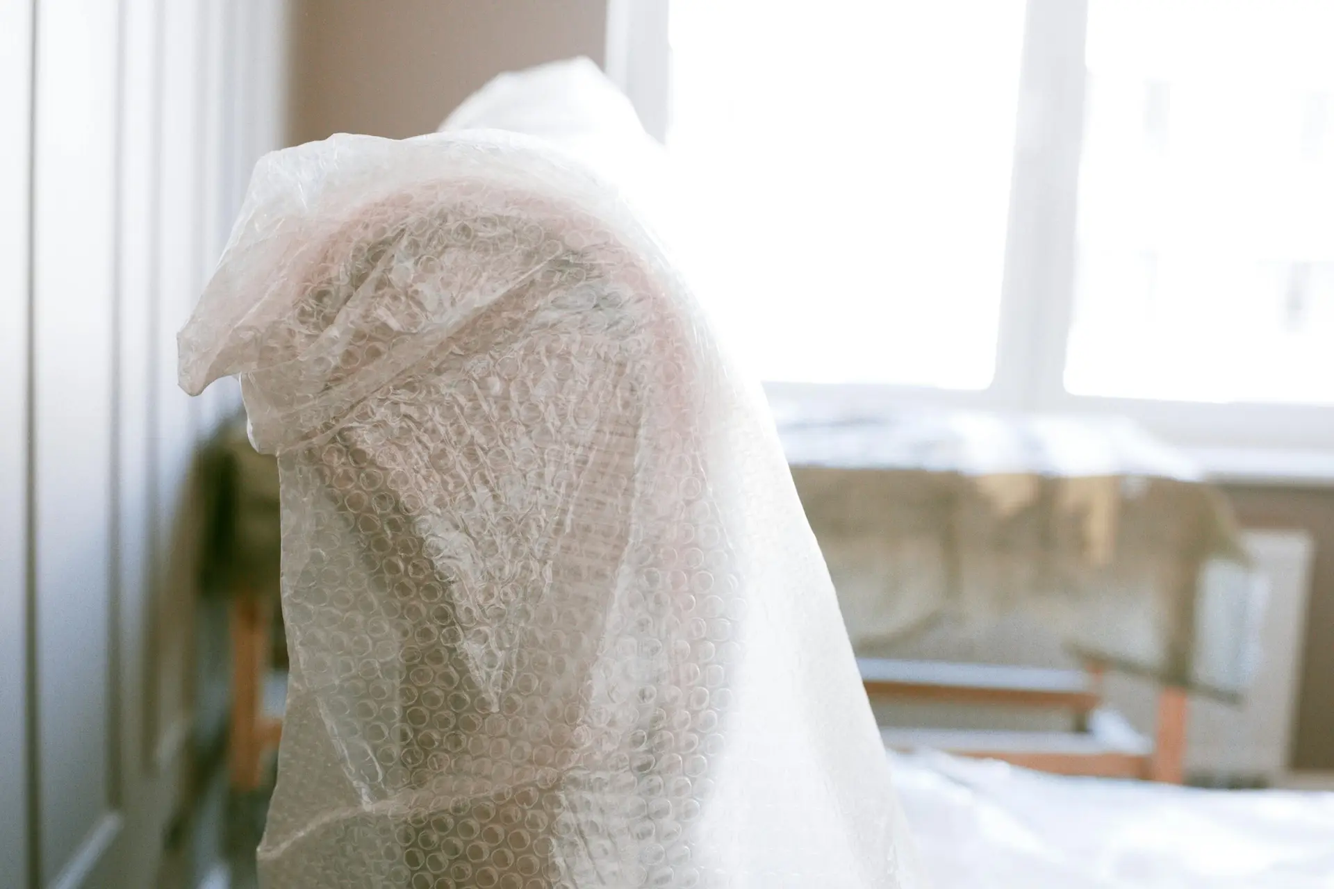 An Urgent Pro house removalists provider in Brisbane wrapping a tall wardrobe in moving blankets and plastic stretch wrap before loading, with professional equipment visible in a realistic local service setting