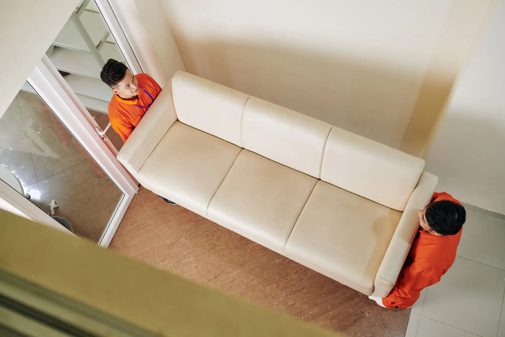 An Urgent Pro house removalists provider in Gold Coast carrying a wrapped sofa out the front door of a home to the waiting removal truck, with professional equipment visible in a realistic local service setting