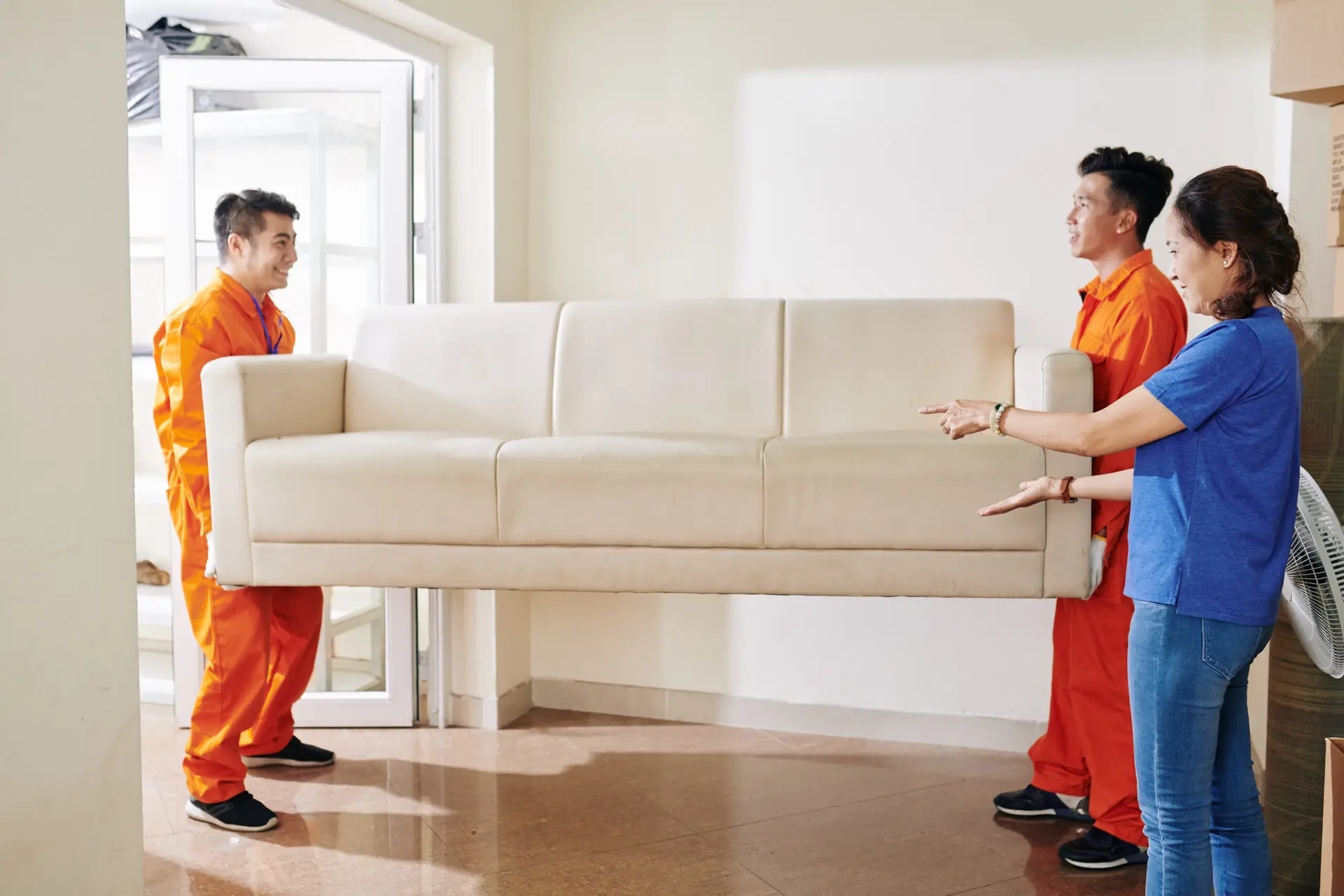 An Urgent Pro house removalists provider in Melbourne carrying a wrapped sofa out the front door of a home to the waiting removal truck, with professional equipment visible in a realistic local service setting