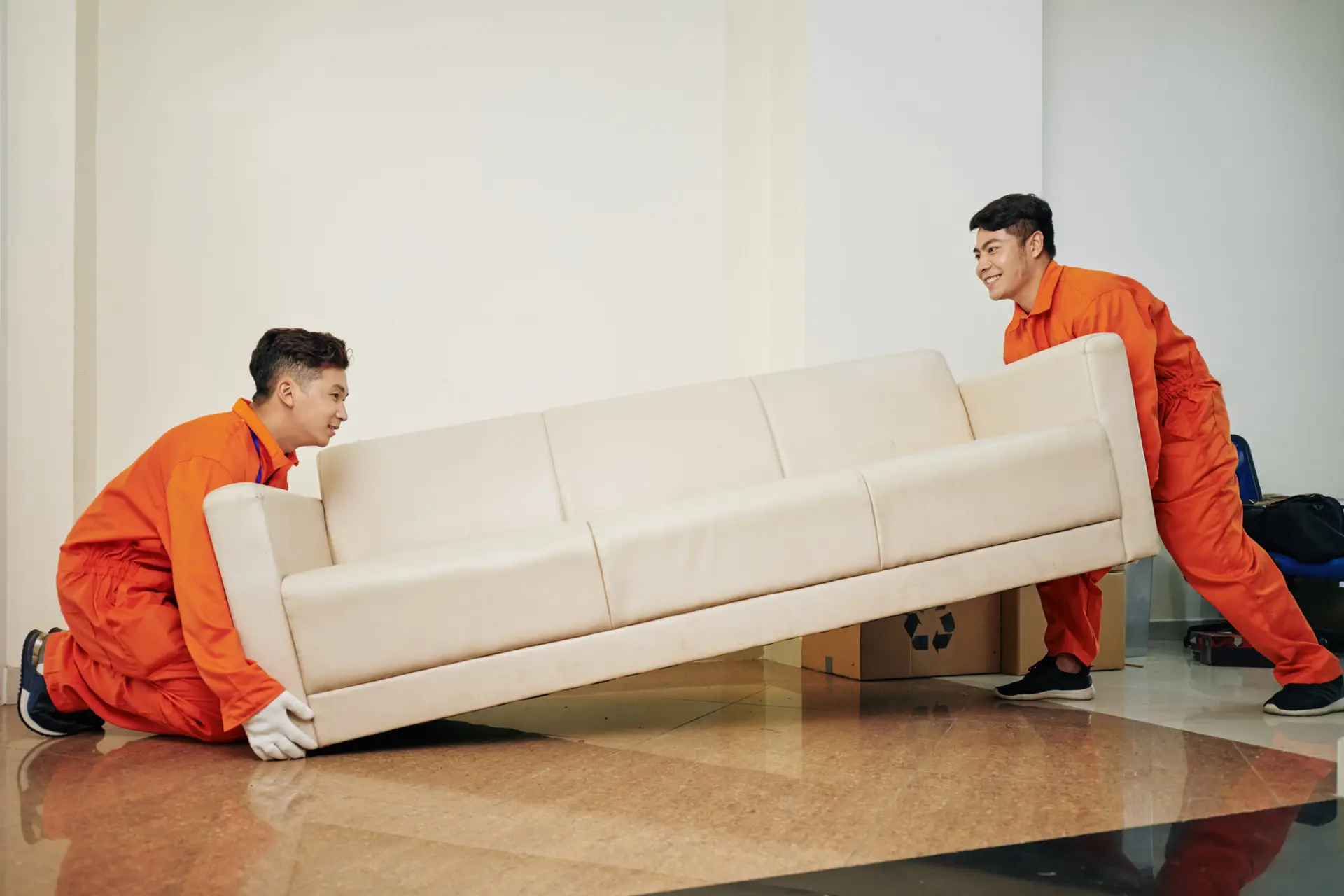 An Urgent Pro house removalists provider in Sydney carrying a wrapped sofa out the front door of a home to the waiting removal truck, with professional equipment visible in a realistic local service setting
