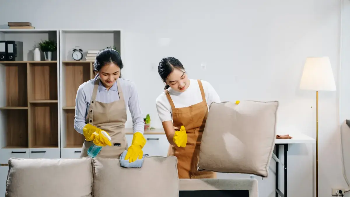 Two cleaning providers working on upholstered furniture in a modern residential living room during an end of lease clean