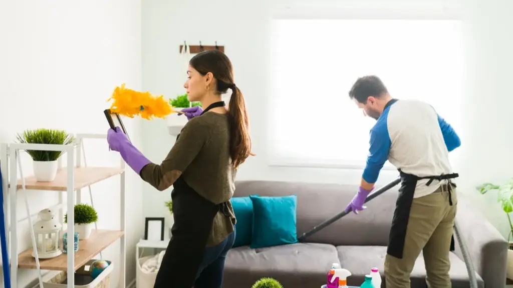 Two professional cleaners dusting and vacuuming a residential living room during a rental property changeover clean