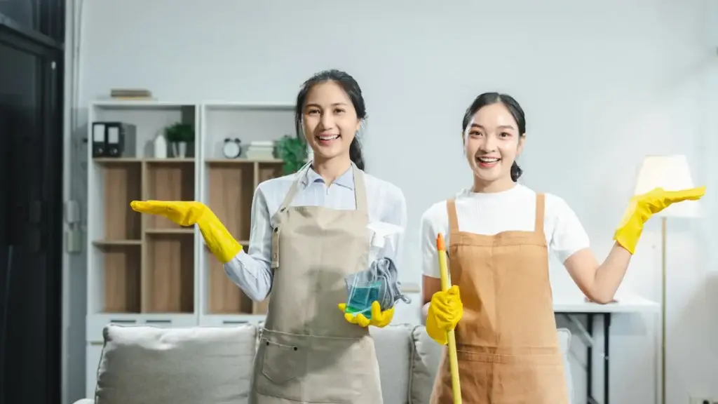 Two professional cleaning providers in aprons and gloves holding equipment in a residential home interior