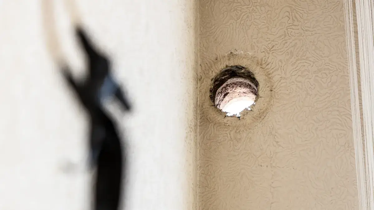 Large ragged hole in a textured render wall showing exposed plasterboard backing