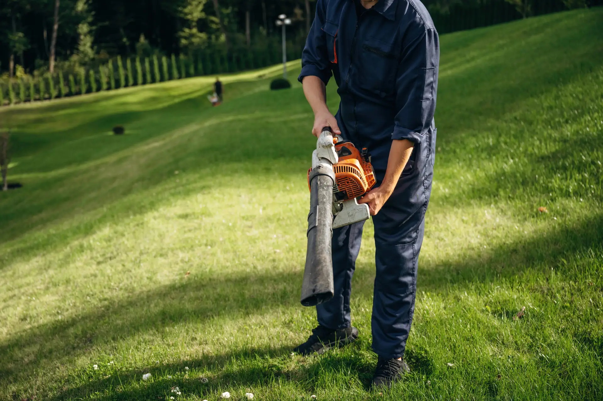 An Urgent Pro lawn mowing provider in Brisbane using a leaf blower to clear grass clippings from the path and driveway after mowing, with professional equipment visible in a realistic local service setting