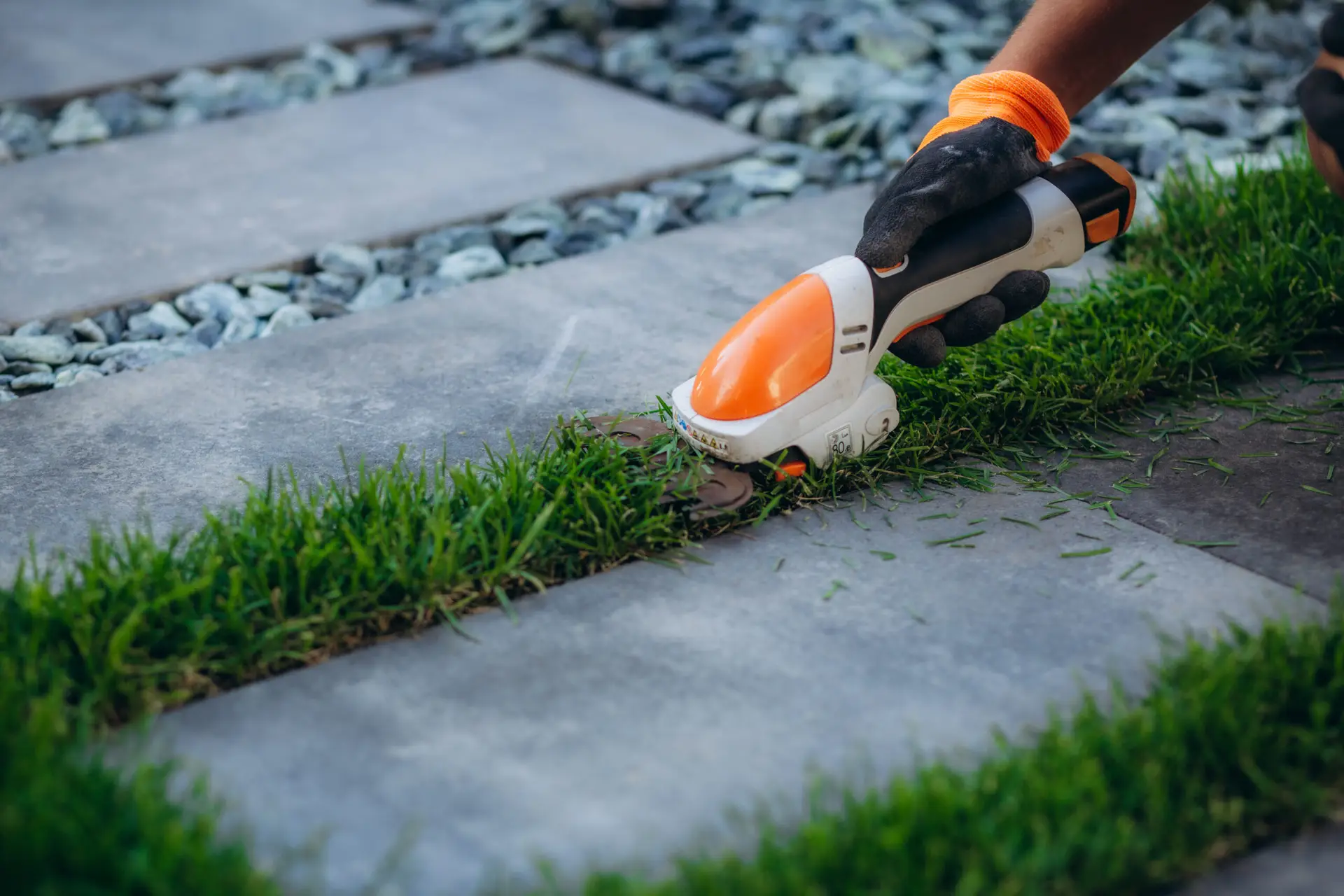 An Urgent Pro lawn mowing provider in Brisbane using a line trimmer to cut clean edges along a concrete path and driveway border, with professional equipment visible in a realistic local service setting