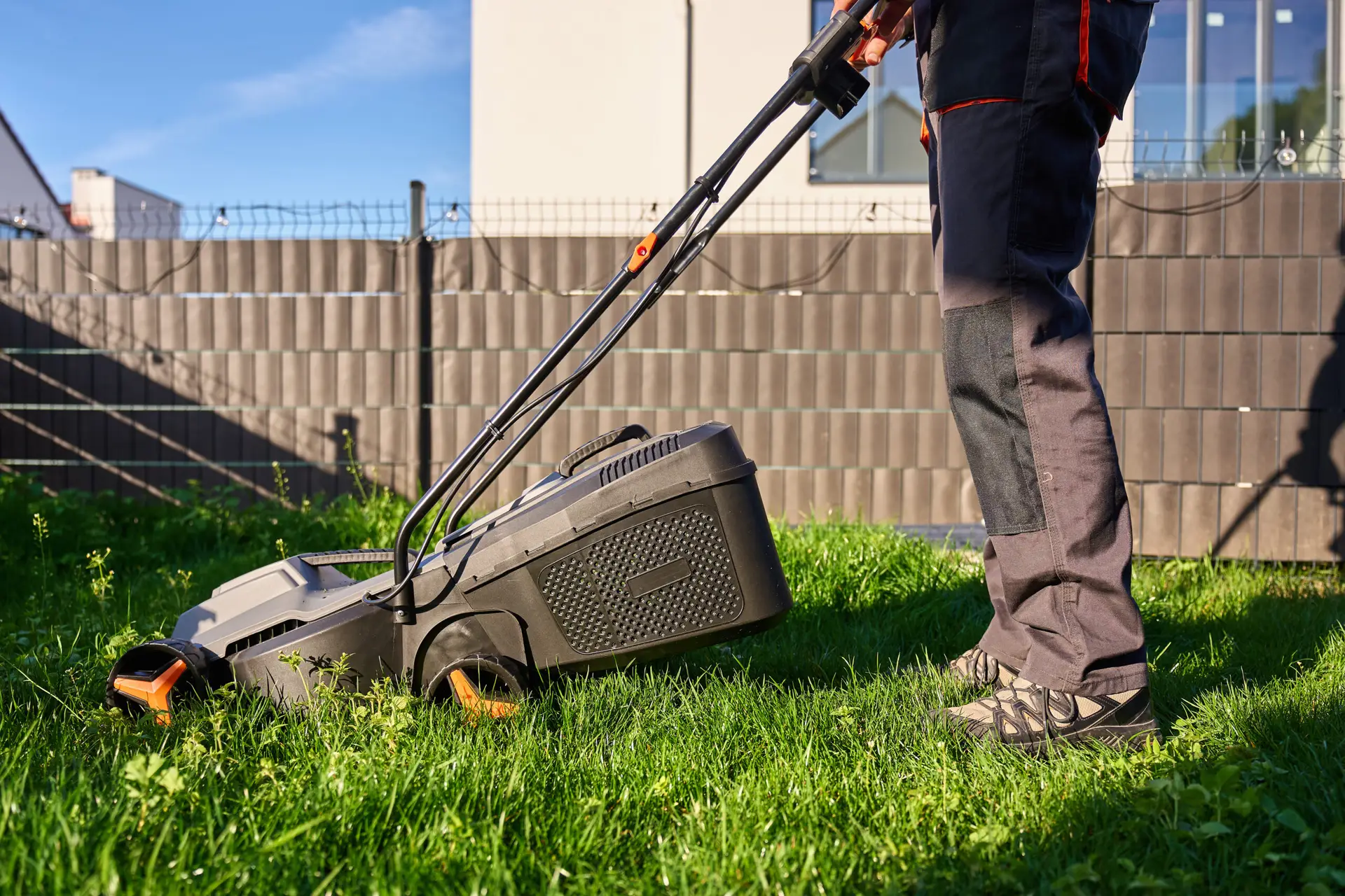An Urgent Pro lawn mowing provider in Brisbane mowing the front lawn of a residential property with a push mower beside the footpath, with professional equipment visible in a realistic local service setting
