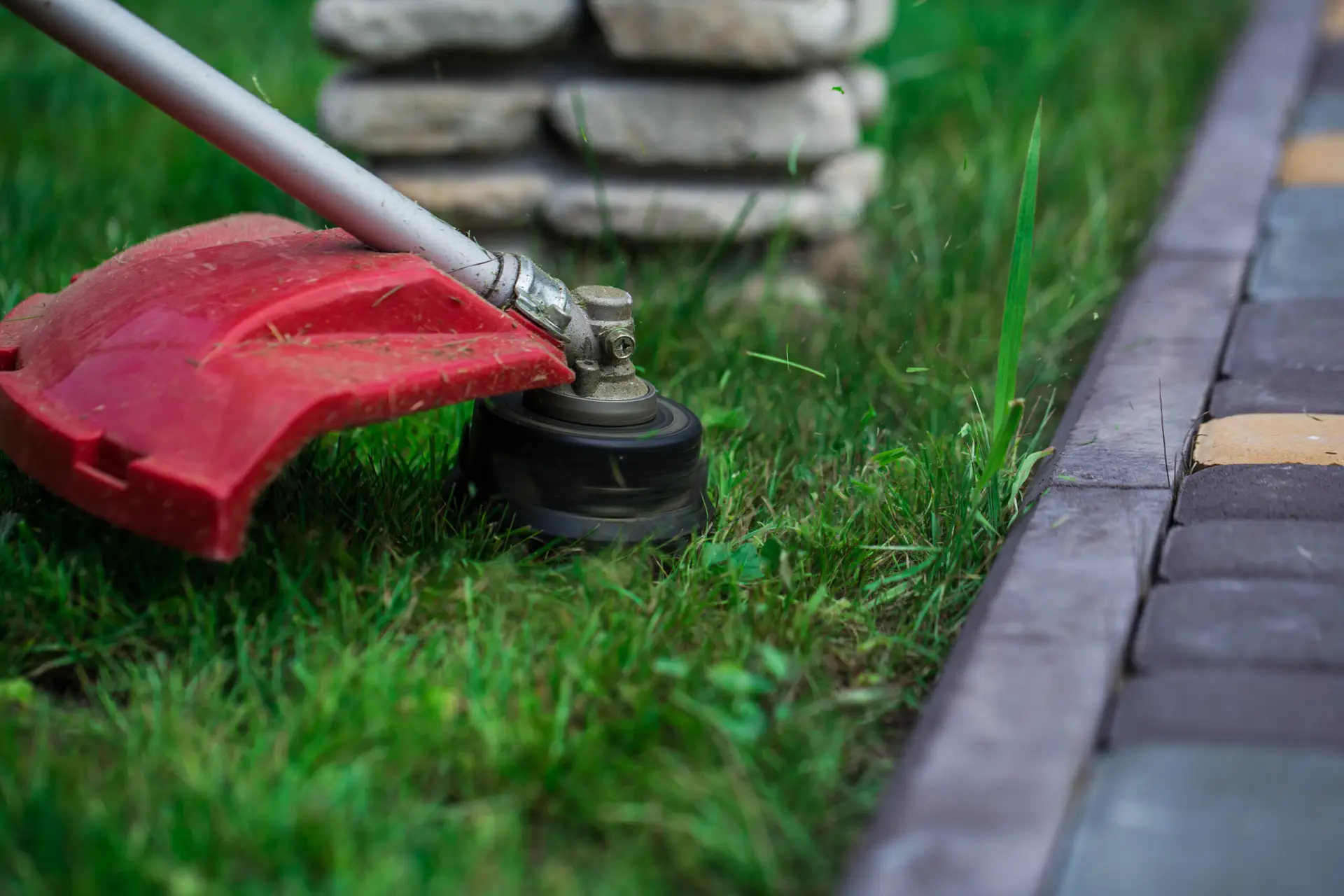 An Urgent Pro lawn mowing provider in Gold Coast using a line trimmer to cut clean edges along a concrete path and driveway border, with professional equipment visible in a realistic local service setting