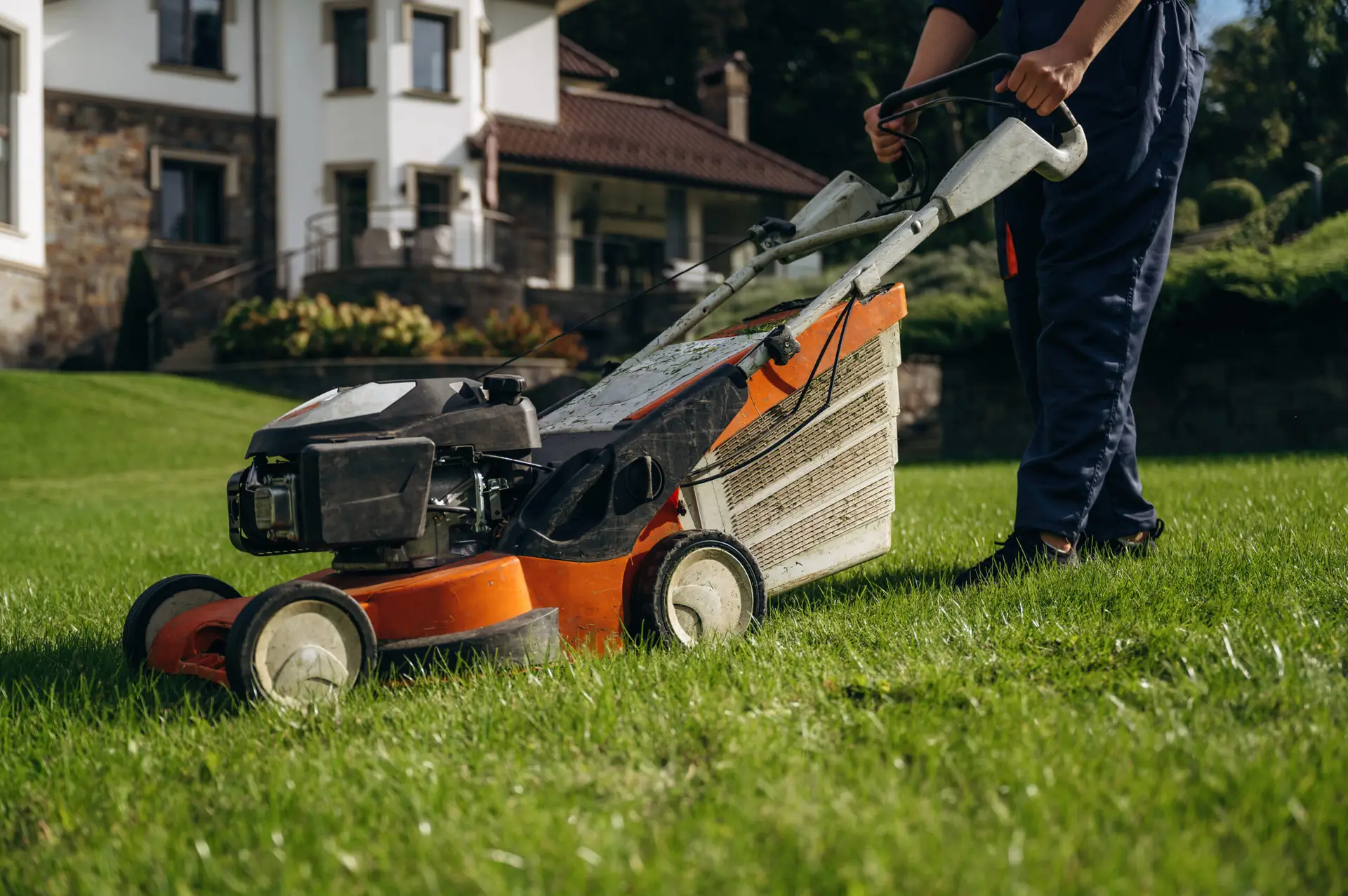An Urgent Pro lawn mowing provider in Gold Coast mowing the front lawn of a residential property with a push mower beside the footpath, with professional equipment visible in a realistic local service setting