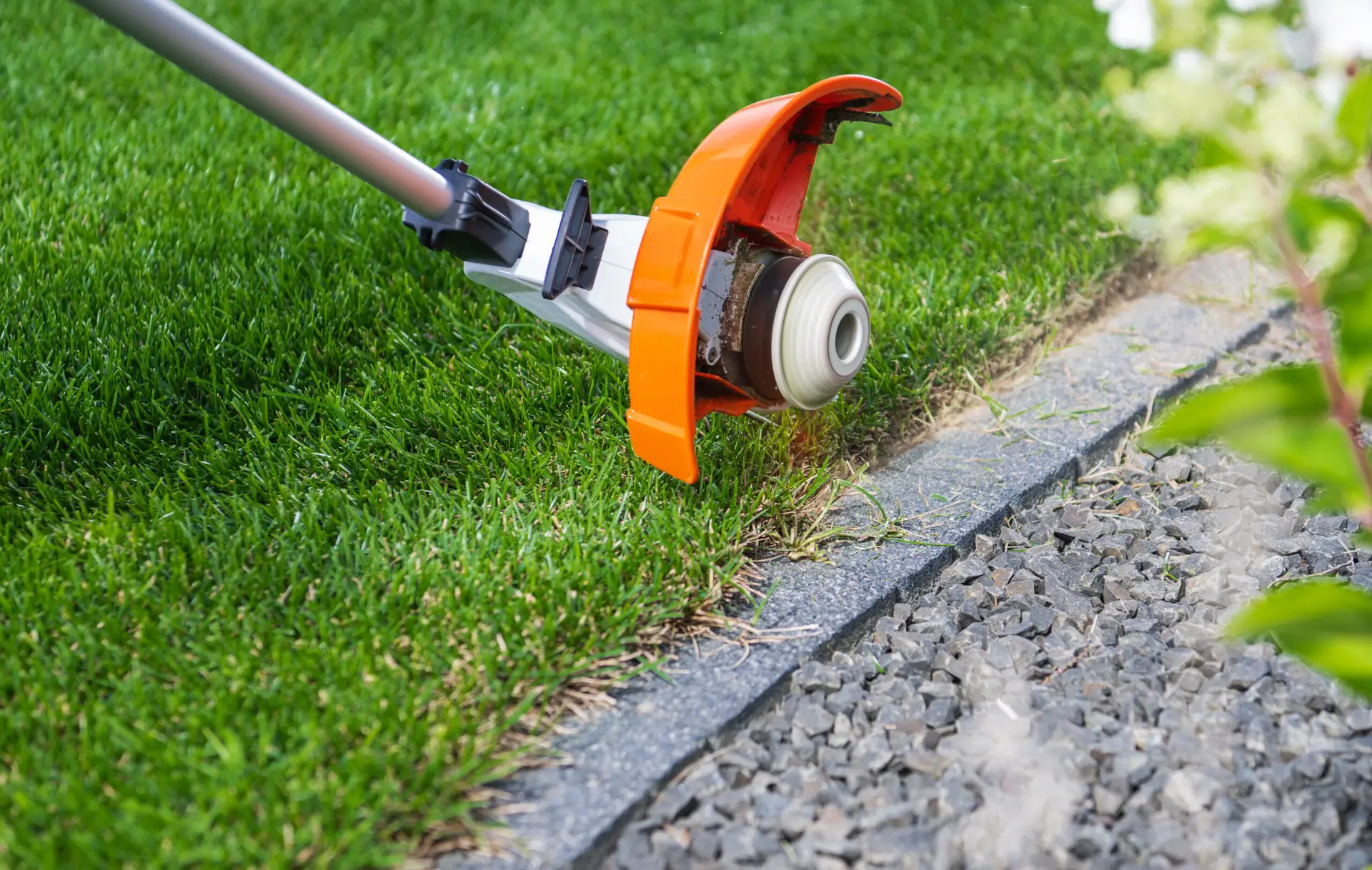 An Urgent Pro lawn mowing provider in Melbourne using a line trimmer to cut clean edges along a concrete path and driveway border, with professional equipment visible in a realistic local service setting