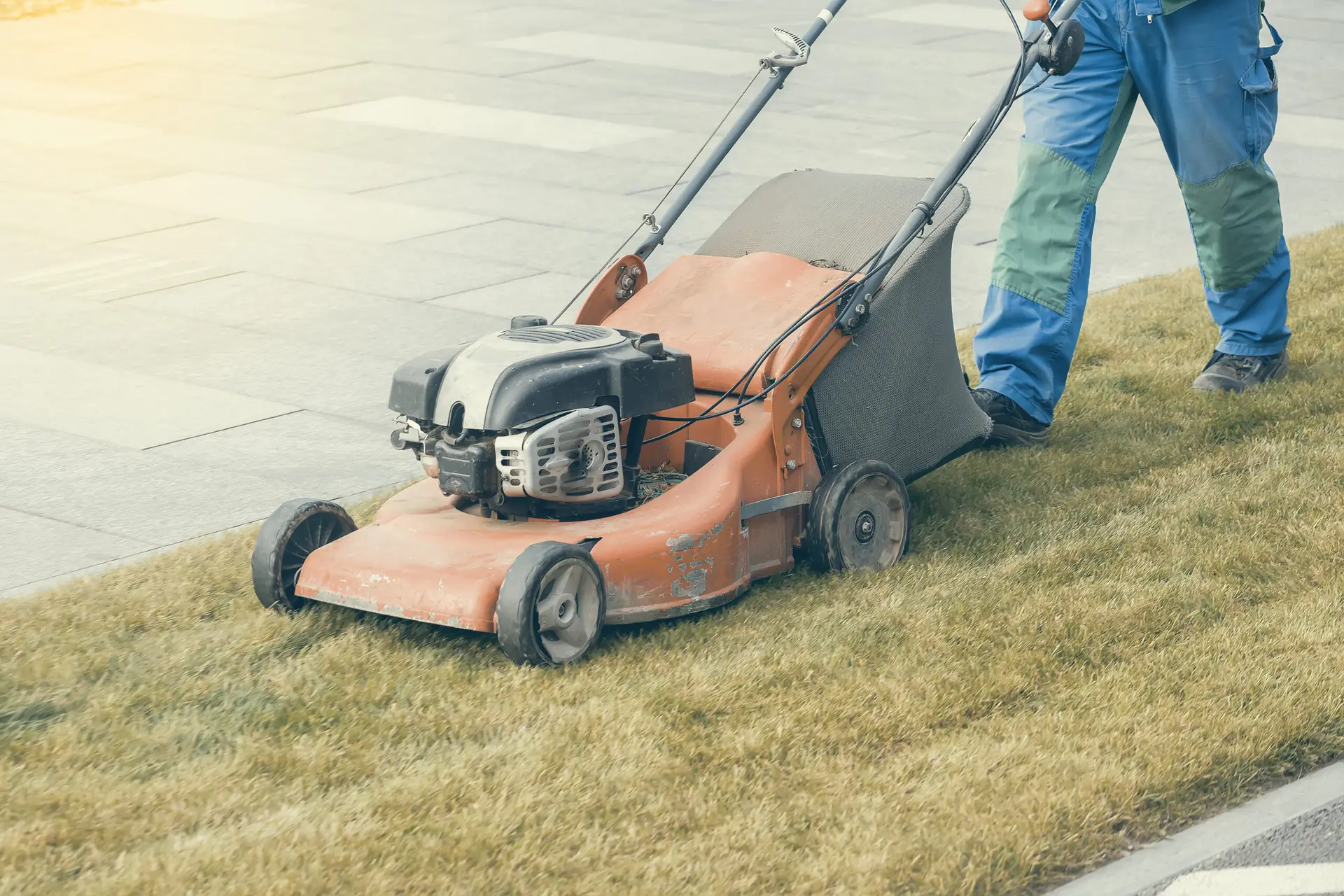 An Urgent Pro lawn mowing provider in Melbourne mowing the front lawn of a residential property with a push mower beside the footpath, with professional equipment visible in a realistic local service setting