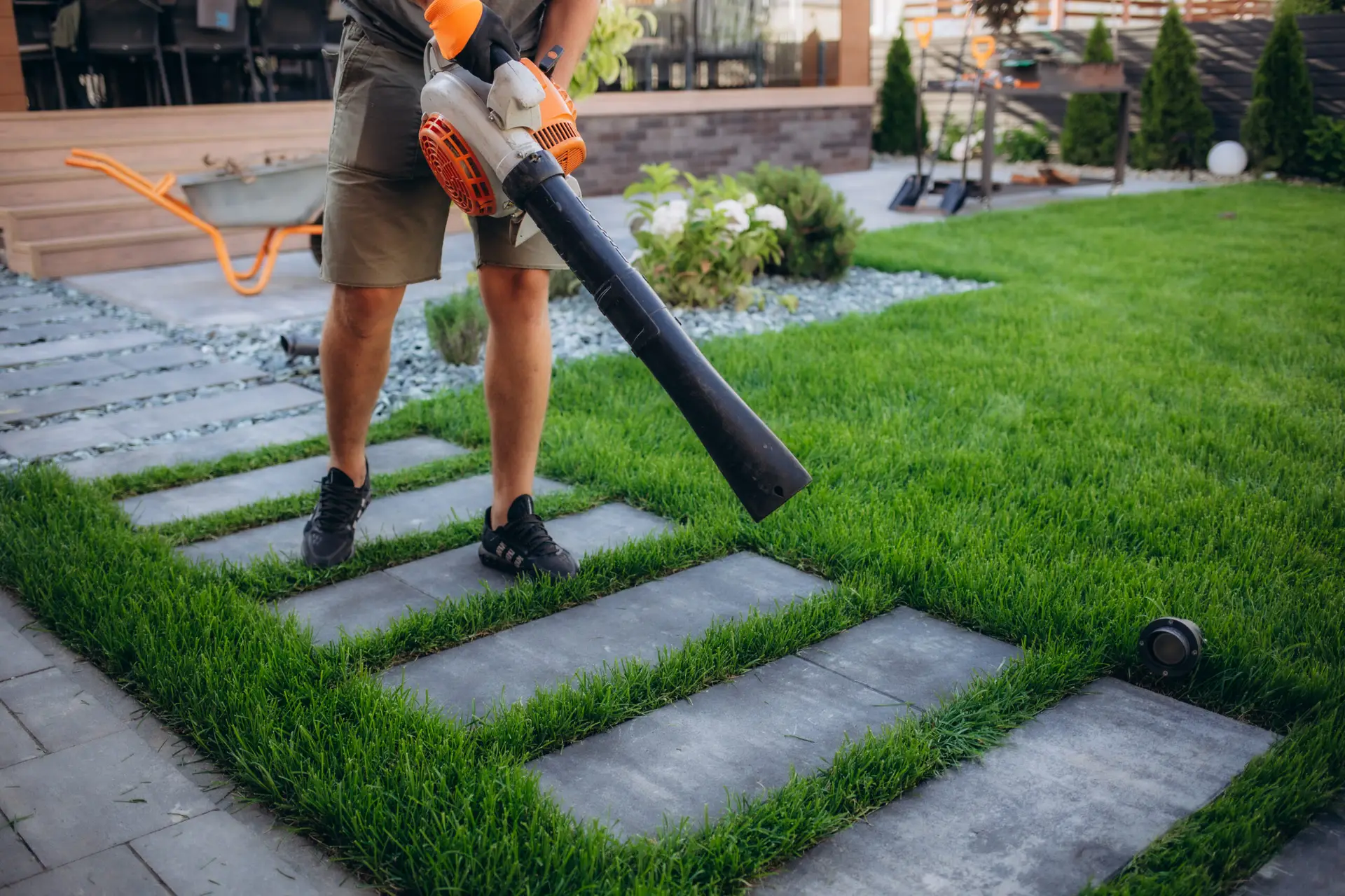 An Urgent Pro lawn mowing provider in Perth using a leaf blower to clear grass clippings from the path and driveway after mowing, with professional equipment visible in a realistic local service setting