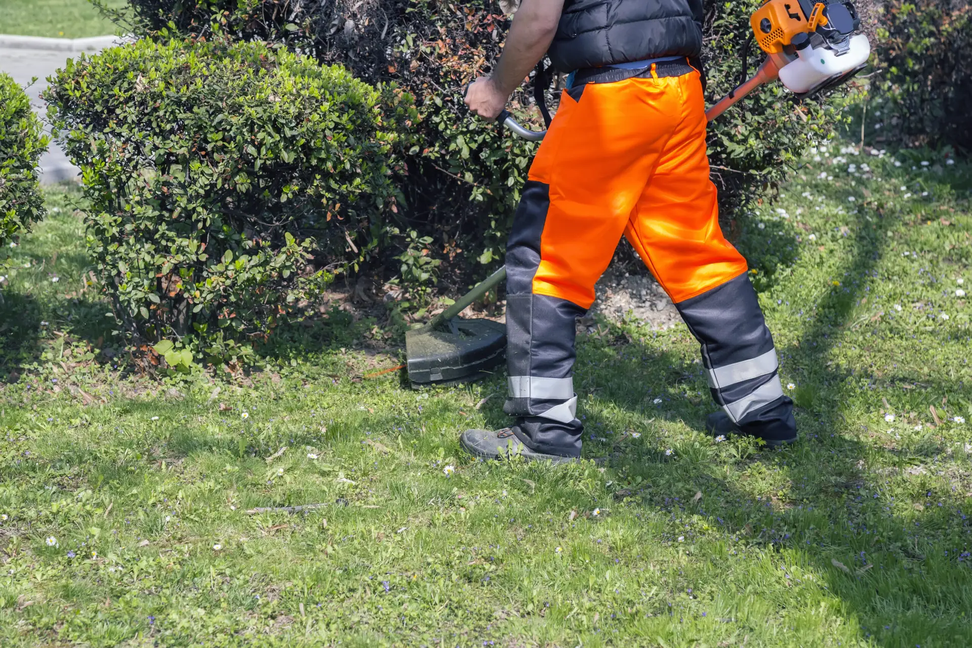 An Urgent Pro lawn mowing provider in Perth using a line trimmer to cut clean edges along a concrete path and driveway border, with professional equipment visible in a realistic local service setting