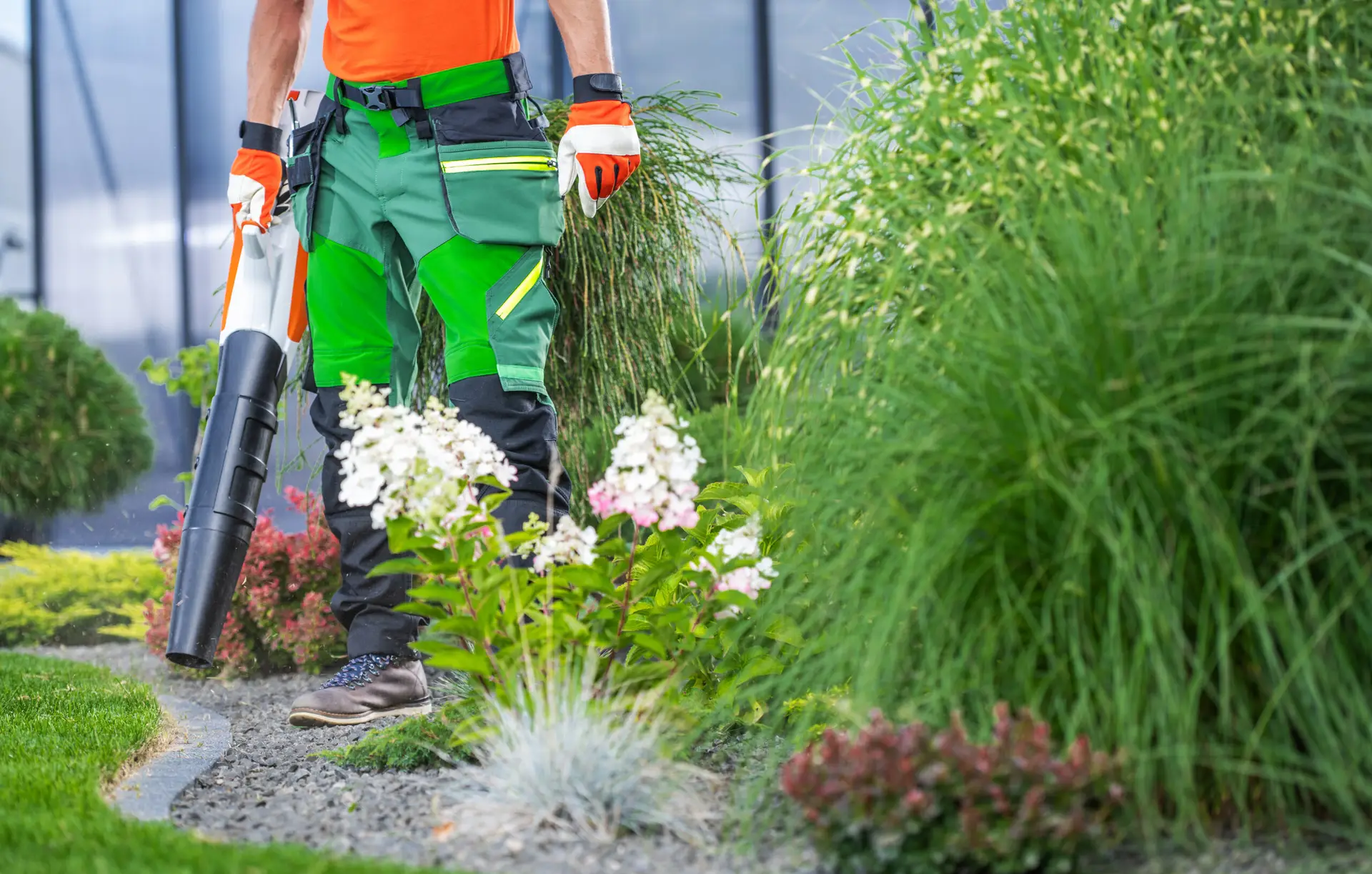 An Urgent Pro lawn mowing provider in Sydney clearing leaf litter and tidying the edges of garden beds with a rake and hand tools, with professional equipment visible in a realistic local service setting