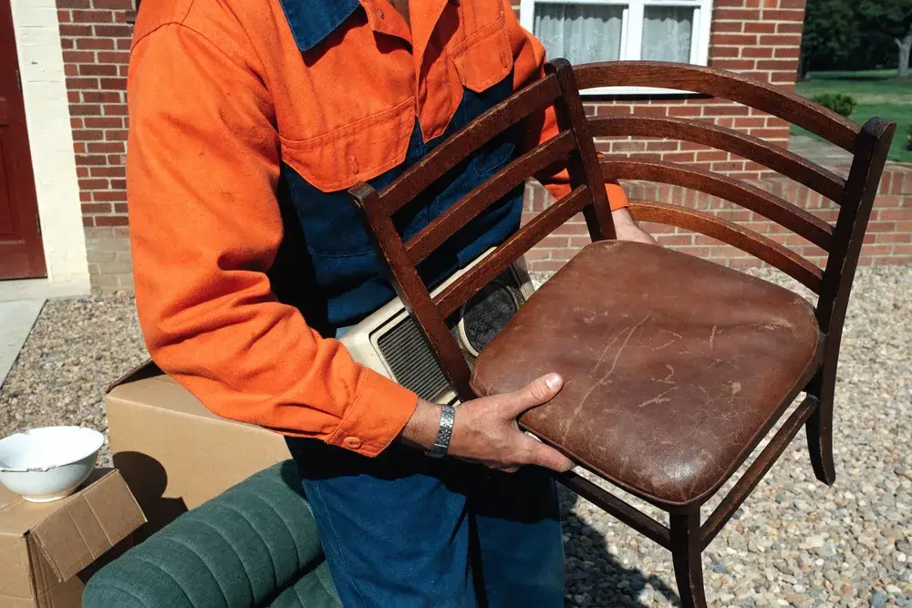 Man in orange jacket holding an old wooden chair outside, Cannington, Perth