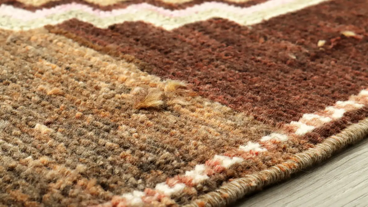 Close-up of patterned area rug pile showing knotted construction and bound edge on light timber floor