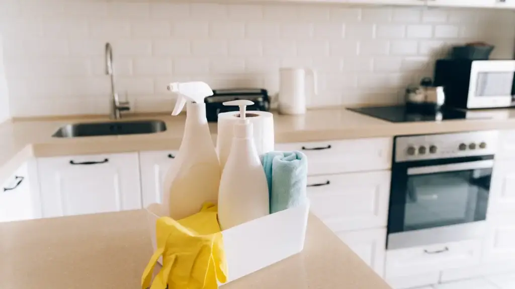 Caddy of cleaning supplies with spray bottle, cloth and yellow gloves on a kitchen benchtop