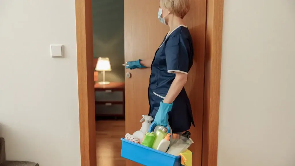Professional cleaner in uniform carrying a caddy of cleaning supplies into a room at a rental property