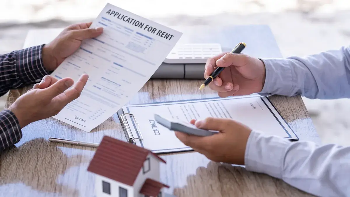 Two people exchanging rental documents including a contract at a table with a house model