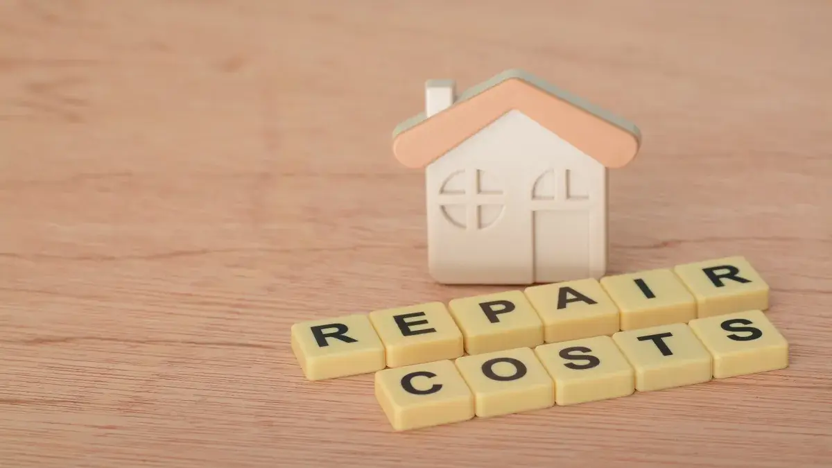 Toy house model with letter tiles spelling REPAIR COSTS on a wooden surface