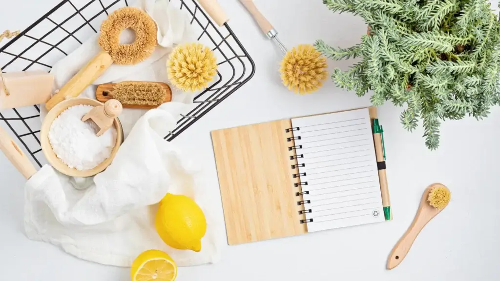 Natural cleaning brushes, baking soda, lemon and a checklist notebook arranged on a white surface