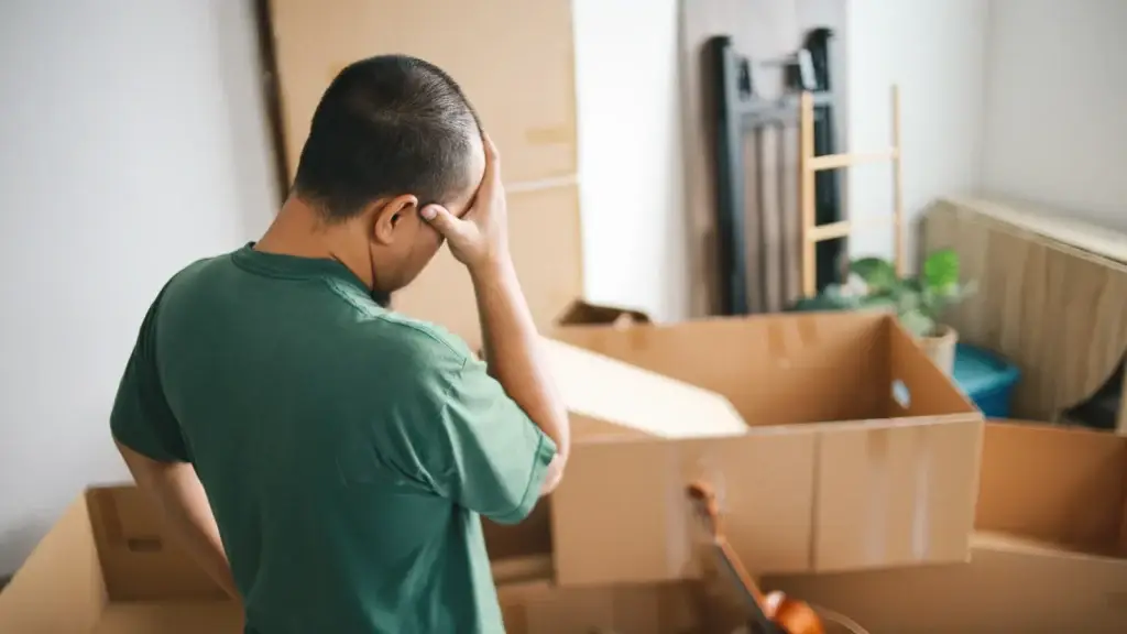 Man sitting with head in hand surrounded by open cardboard moving boxes, stressed on moving day