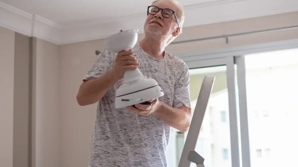 Man on ladder inspecting a ceiling fan fitting inside an Australian home