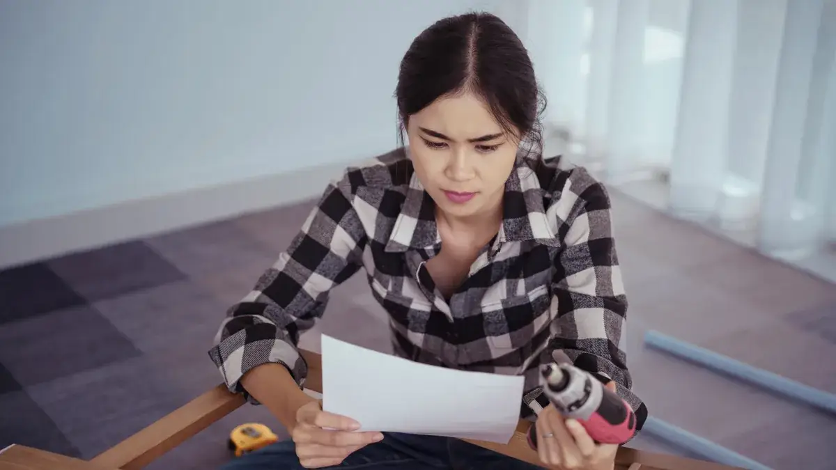 Woman reading repair instructions while holding a power drill during a DIY task