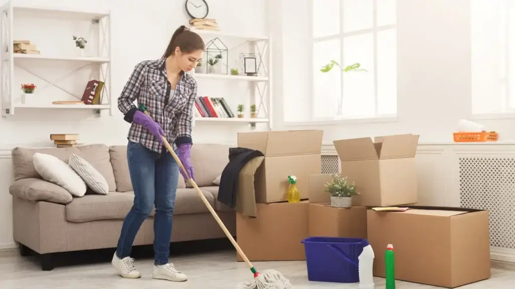 Tenant mopping floor during a move-out clean in a furnished living room with packing boxes